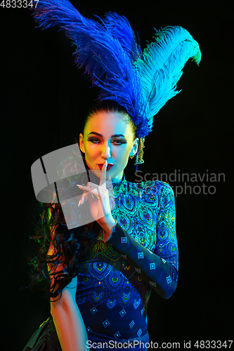 Image of Beautiful young woman in carnival and masquerade costume in colorful neon lights on black background