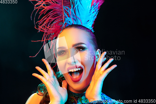 Image of Beautiful young woman in carnival and masquerade costume in colorful neon lights on black background