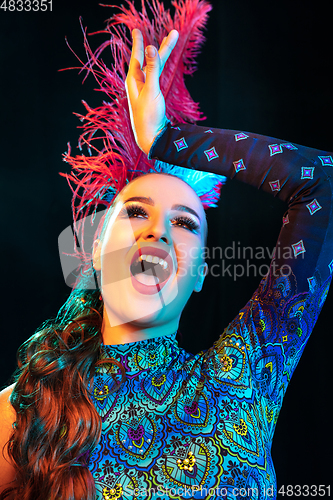 Image of Beautiful young woman in carnival and masquerade costume in colorful neon lights on black background