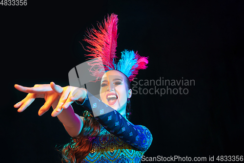 Image of Beautiful young woman in carnival and masquerade costume in colorful neon lights on black background