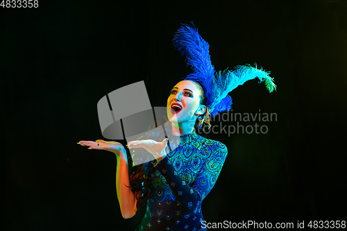 Image of Beautiful young woman in carnival and masquerade costume in colorful neon lights on black background