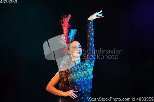 Image of Beautiful young woman in carnival and masquerade costume in colorful neon lights on black background