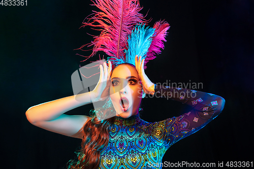 Image of Beautiful young woman in carnival and masquerade costume in colorful neon lights on black background