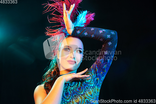 Image of Beautiful young woman in carnival and masquerade costume in colorful neon lights on black background