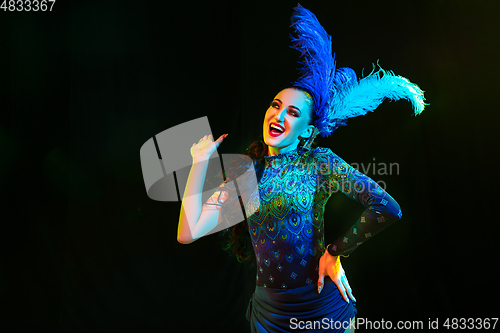 Image of Beautiful young woman in carnival and masquerade costume in colorful neon lights on black background