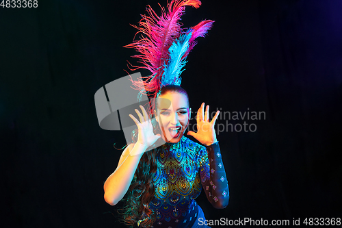 Image of Beautiful young woman in carnival and masquerade costume in colorful neon lights on black background