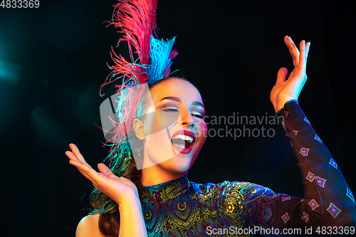 Image of Beautiful young woman in carnival and masquerade costume in colorful neon lights on black background