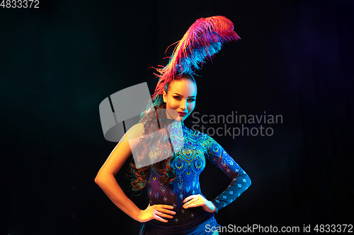 Image of Beautiful young woman in carnival and masquerade costume in colorful neon lights on black background