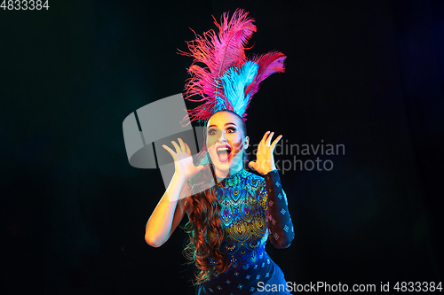 Image of Beautiful young woman in carnival and masquerade costume in colorful neon lights on black background