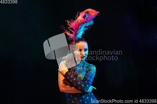 Image of Beautiful young woman in carnival and masquerade costume in colorful neon lights on black background