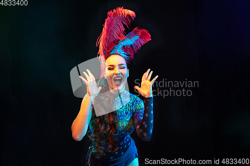 Image of Beautiful young woman in carnival and masquerade costume in colorful neon lights on black background