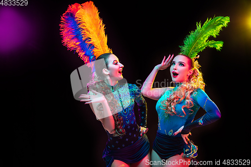 Image of Beautiful young women in carnival and masquerade costume in colorful neon lights on black background