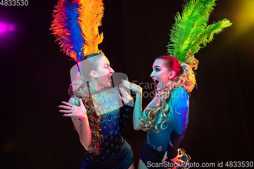 Image of Beautiful young women in carnival and masquerade costume in colorful neon lights on black background