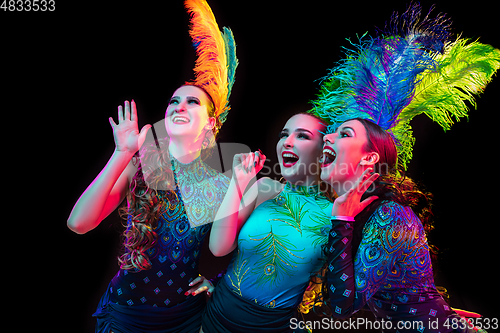 Image of Beautiful young women in carnival and masquerade costume in colorful neon lights on black background