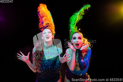 Image of Beautiful young women in carnival and masquerade costume in colorful neon lights on black background