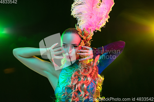 Image of Beautiful young woman in carnival and masquerade costume in colorful neon lights on black background