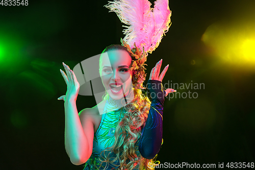 Image of Beautiful young woman in carnival and masquerade costume in colorful neon lights on black background