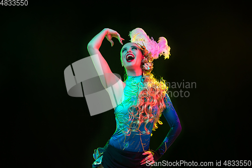 Image of Beautiful young woman in carnival and masquerade costume in colorful neon lights on black background