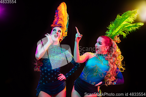 Image of Beautiful young women in carnival and masquerade costume in colorful neon lights on black background