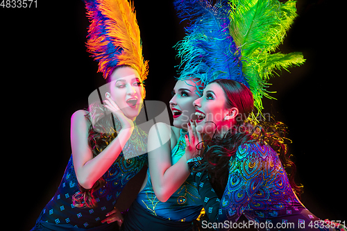 Image of Beautiful young women in carnival and masquerade costume in colorful neon lights on black background