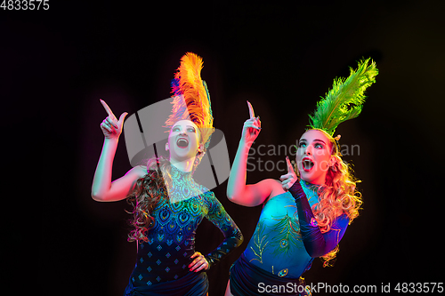 Image of Beautiful young women in carnival and masquerade costume in colorful neon lights on black background