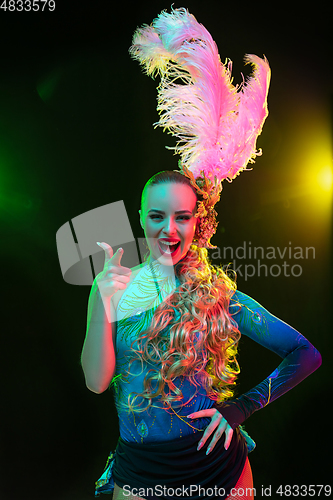 Image of Beautiful young woman in carnival and masquerade costume in colorful neon lights on black background