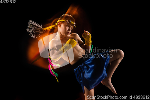 Image of Little boy exercising thai boxing on black background. Fighter practicing, training in martial arts in action, motion. Evolution of movement, catching moment.