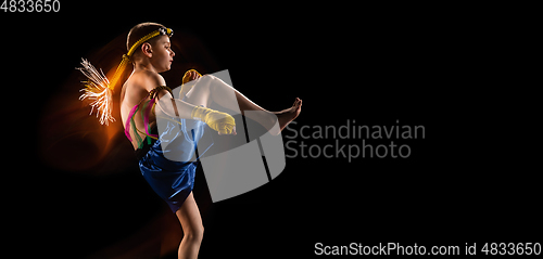 Image of Little boy exercising thai boxing on black background. Fighter practicing, training in martial arts in action, motion. Evolution of movement, catching moment.