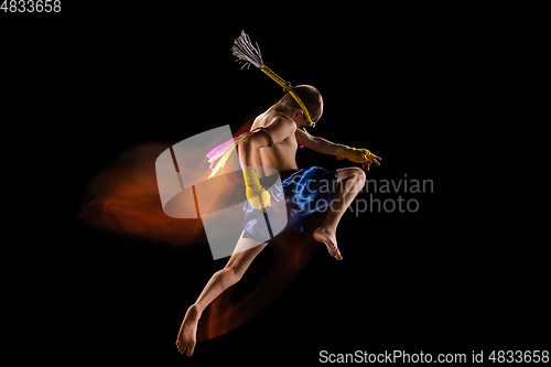 Image of Little boy exercising thai boxing on black background. Fighter practicing, training in martial arts in action, motion. Evolution of movement, catching moment.