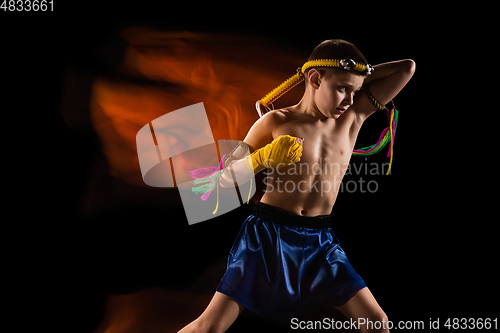 Image of Little boy exercising thai boxing on black background. Fighter practicing, training in martial arts in action, motion. Evolution of movement, catching moment.