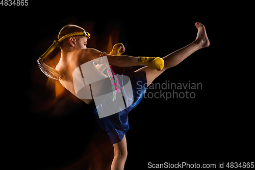 Image of Little boy exercising thai boxing on black background. Fighter practicing, training in martial arts in action, motion. Evolution of movement, catching moment.