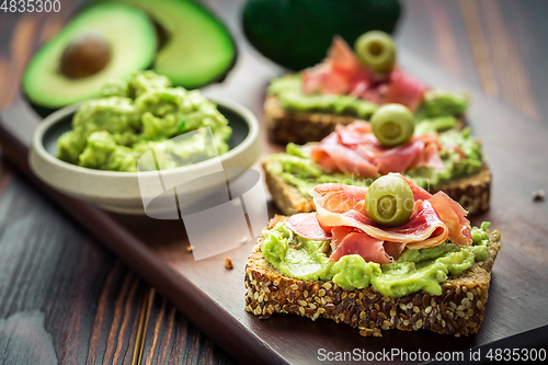 Image of Guacamole dip or spread with open sandwiches and ham on wooden kitchen table