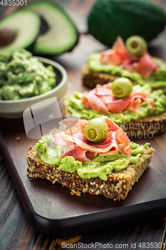 Image of Guacamole dip or spread with open sandwiches and ham on wooden kitchen table
