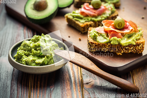 Image of Guacamole dip or spread with open sandwiches and ham on wooden kitchen table