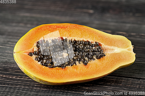 Image of Half papaya on a wooden table. Papaya lies on dark boards