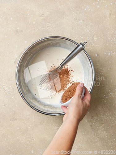 Image of cocoa powder is added to the whipped eggs and sugar in a metal b