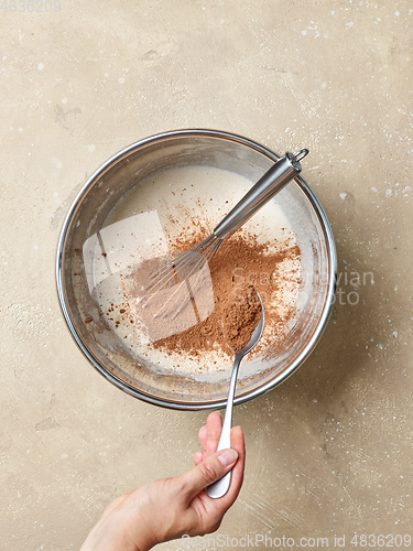 Image of cocoa powder is added to the whipped eggs and sugar in a metal b