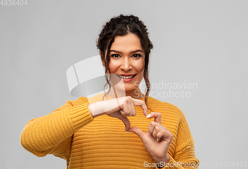 Image of smiling young woman making hand heart gesture