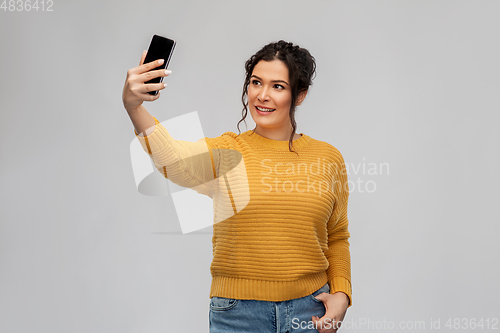 Image of smiling young woman taking selfie by smartphone