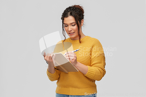 Image of happy young woman writing to diary or notebook