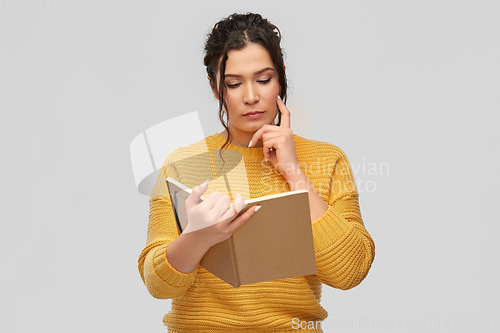 Image of pensive young woman reading diary or notebook