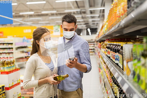 Image of couple in masks with phone and olive oil at store