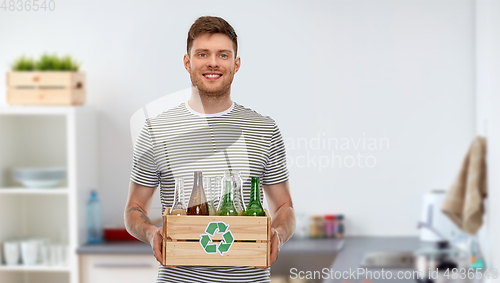 Image of smiling young man sorting glass waste at home