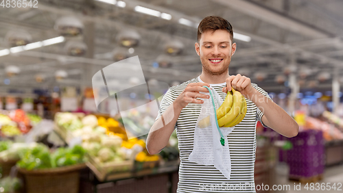 Image of smiling man putting bananas into reusable net bag