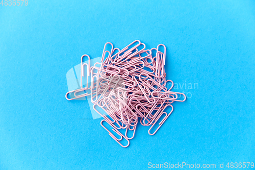 Image of heap of pink office clips on blue background