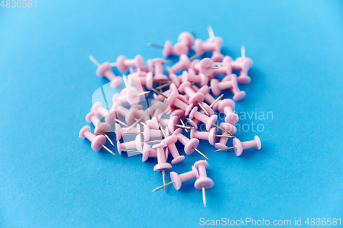 Image of heap of pink office pins on blue background