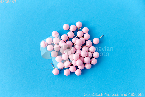 Image of heap of pink office pins on blue background