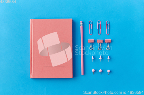 Image of pink notebook, pins, clips and pencil on blue