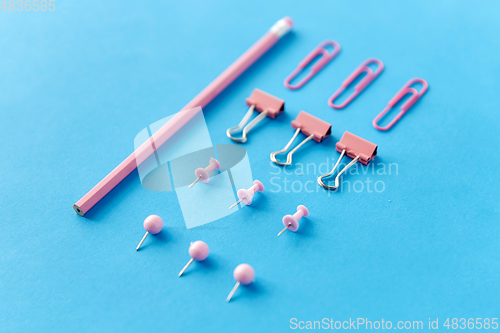 Image of pink pencil, pins and clips on blue background