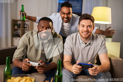 Image of happy friends playing video games at home at night